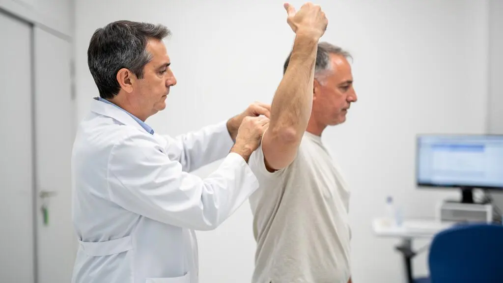 Chirurgien orthopédiste effectuant un test de mobilité de l'épaule sur un patient debout lors d'un examen clinique